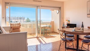 A balcony with a view of the sea, a dining area with a table and chairs, and a sofa with a cushion. - The sound of the waves (Port-la-Nouvelle)
