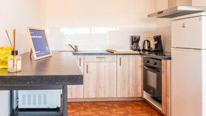 A modern kitchen with wooden cabinets, a black countertop, a coffee maker, and a built-in oven. - The sound of the waves (Port-la-Nouvelle)