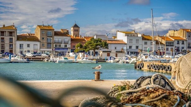 A marina with boats docked, buildings with traditional architecture, and a clear sky. - The sound of the waves (Port-la-Nouvelle)