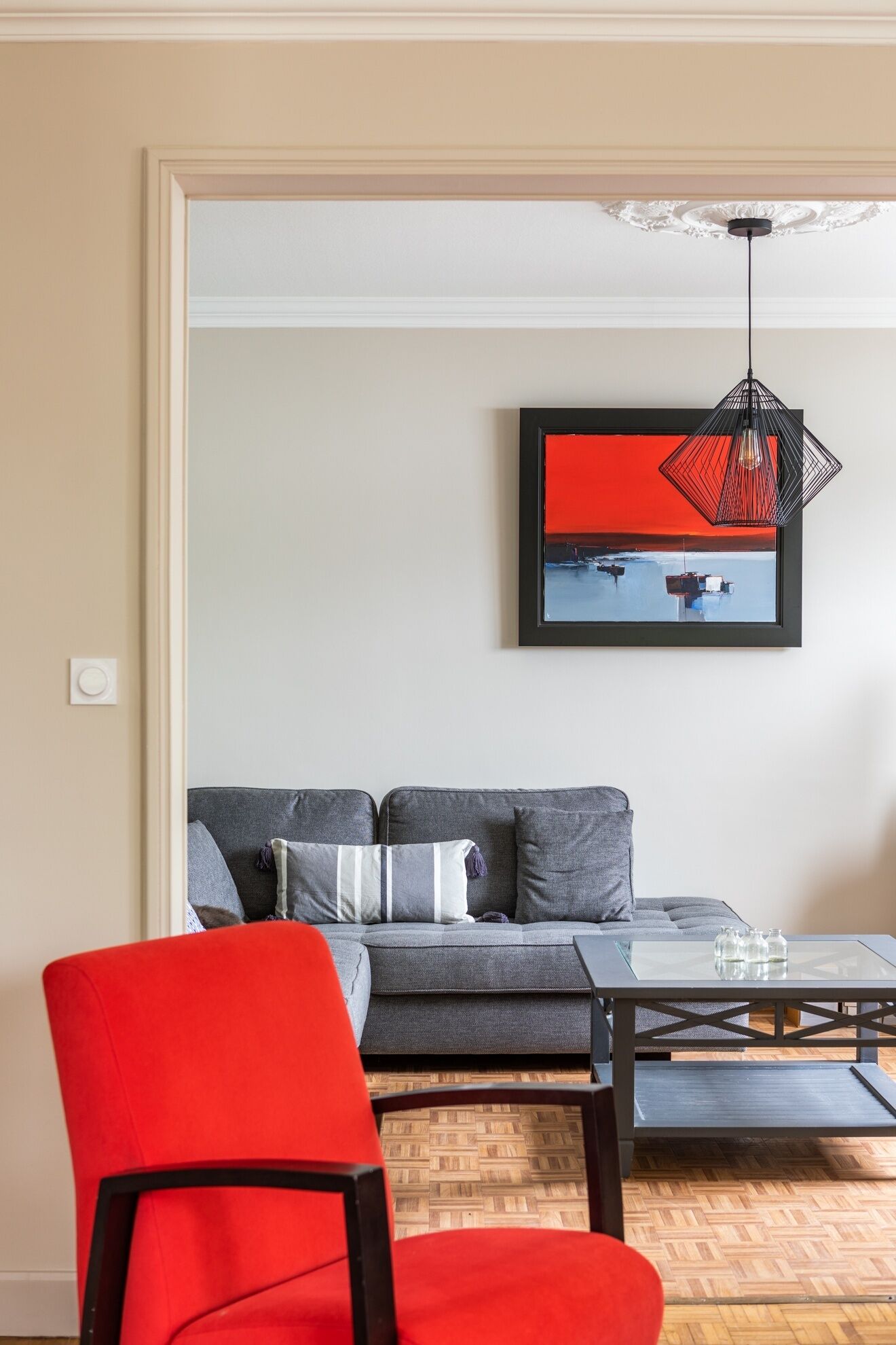 Una sala de estar moderna con un sofá gris, un sillón rojo y una mesa de centro de vidrio.