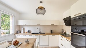 Una cocina moderna con armarios blancos, encimera de madera, horno empotrado y lámpara colgante.