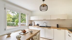 Una cocina moderna con encimera de madera, armarios blancos, un ventanal grande y una lámpara colgante.
