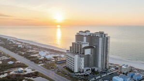 Un hôtel de grande hauteur, avec de nombreux étages, situé près d’une plage offrant une vue sur le coucher de soleil.