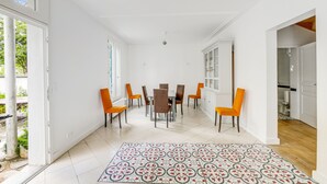 A spacious dining area with a white tiled floor, a patterned rug, and orange chairs around a central table.