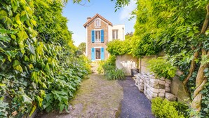 A stone wall with a garden path leading to a house with blue shutters.