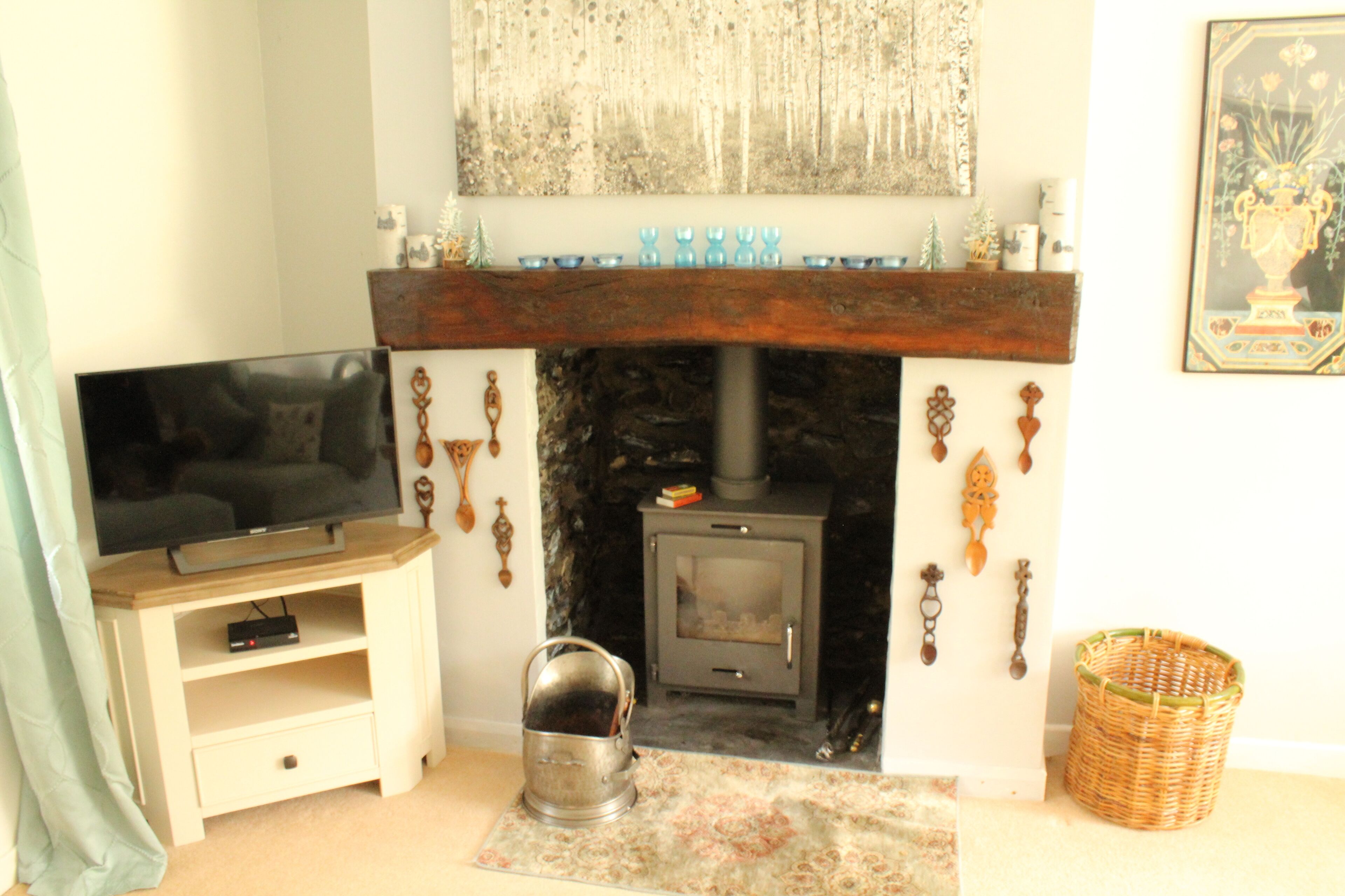 A living room with a television on a wooden stand, a fireplace with a stone surround, and a decorative wall piece above it.