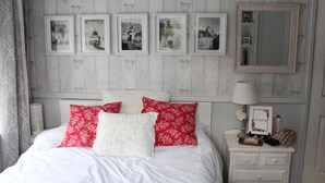 Una camera da letto ordinata con un letto, cuscini, un comodino con una lampada, uno specchio e quadri appesi al muro.
