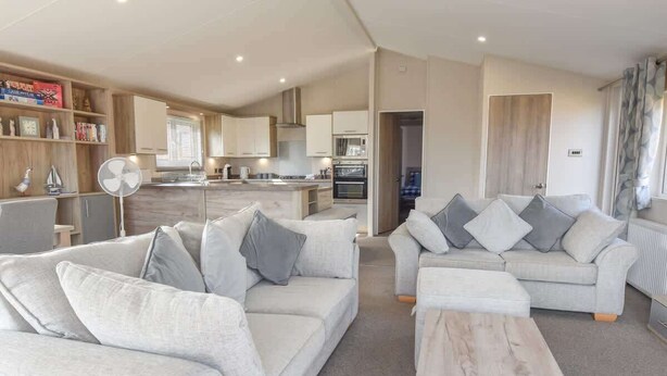 A modern living room with a sofa, a coffee table, and a kitchen area in the background. - Rowan a welcoming countryside lodge (Ryde)