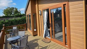 A wooden deck with outdoor furniture, a sliding glass door, and a view of the surrounding greenery. - Rowan a welcoming countryside lodge (Ryde)