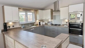 A modern kitchen with a central island, stainless steel appliances, and light-colored cabinetry. - Rowan a welcoming countryside lodge (Ryde)
