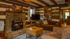 Acogedor interior de una cabaña de madera con chimenea de piedra, televisor y asientos cómodos.