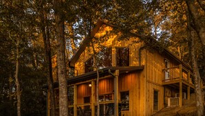 A wooden cabin with a balcony and large windows, surrounded by trees. - Bufflehead | Cabin on the South Holston River (Bristol)