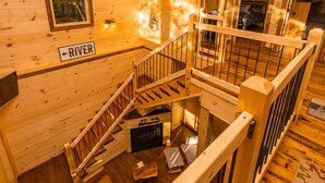 A wooden cabin interior with a staircase, a fireplace, and a bed. - Bufflehead | Cabin on the South Holston River (Bristol)