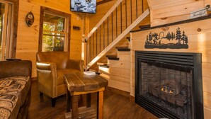 A cozy cabin interior with a wooden staircase, leather armchair, and a fireplace. - Bufflehead | Cabin on the South Holston River (Bristol)