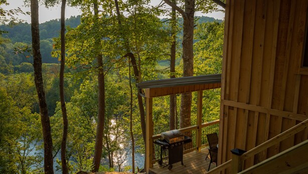 Eine Holzhütte mit einer Terrasse mit Blick auf einen Wald und ein Gewässer.