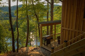 Une cabane en bois dotée d’une terrasse offrant une vue sur une zone boisée et un plan d’eau.