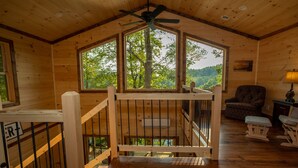 Ein Holzhütten-Interieur mit Balkon, großen Fenstern und einem Deckenventilator.