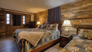 Un dormitorio con pared de madera, una cama con colcha, dos mesitas de noche con lámparas y una ventana con cortinas.