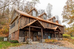 A rustic wooden house with a stone foundation, a covered porch, and a gravel driveway.