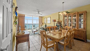 A dining area with a glass-top table, wooden chairs, and a wooden cabinet with glass doors. - Laguna Keyes PH 6 -Oceanfront 3BR-Amazing Views (North Myrtle Beach)