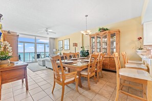 A spacious dining area with a large table, wooden chairs, and a view of the ocean through the sliding glass doors.