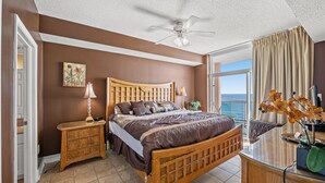 A bedroom with a wooden bed, bedside tables, a ceiling fan, a window with curtains, and a view of the ocean. - Laguna Keyes PH 6 -Oceanfront 3BR-Amazing Views (North Myrtle Beach)