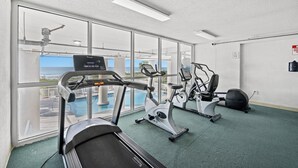 A gym with treadmills, stationary bikes, and a rowing machine, large windows, and a view of a pool.