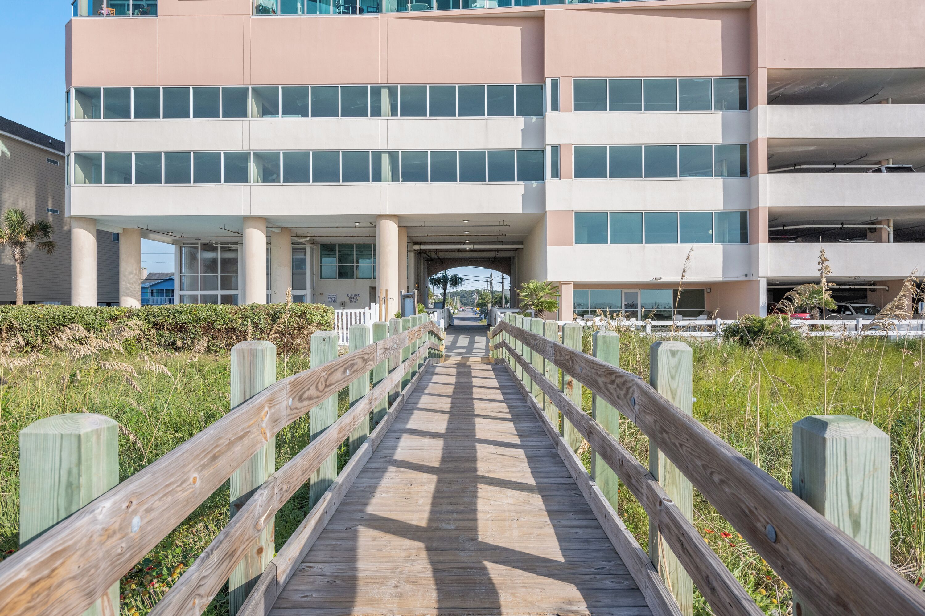 A wooden boardwalk leading to a modern building with multiple floors and large windows.