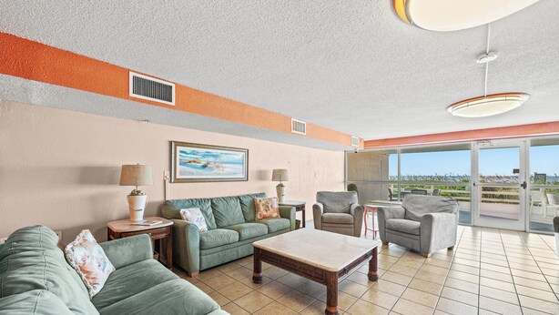 A spacious living room with a green sofa set, a coffee table, and a view through large sliding glass doors to the outside.