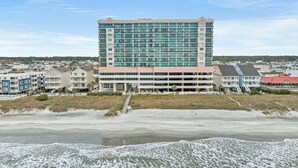 Ein mehrstöckiges Hotel mit Tiefgarage in Strandnähe, wo Wellen auf das Ufer treffen.