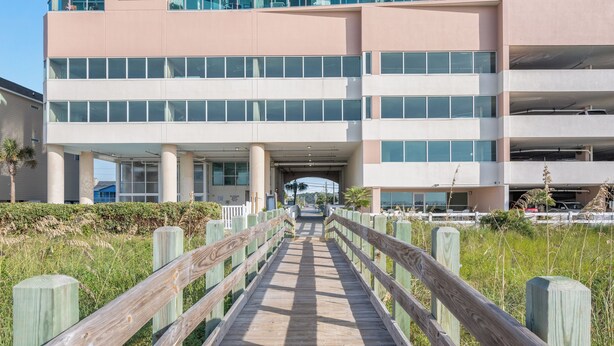 Un muelle de madera que conduce a un edificio moderno de varios pisos y grandes ventanales.