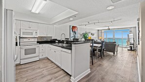 Une cuisine moderne avec des meubles blancs, un grand îlot central et une vue sur l’océan.
