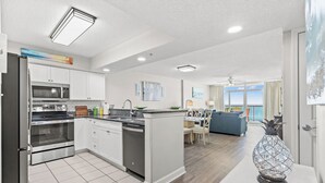 A modern kitchen with white cabinets, stainless steel appliances, and a dining area with a blue sofa.