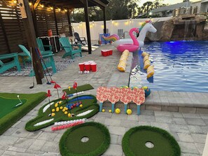 Un patio trasero con piscina, un flamenco inflable y un campo de mini golf.