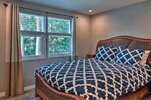 A bedroom with a wooden bed, a large window with blinds, and a view of greenery outside. - *Charming 2bed 2 bath 6 mins from IMG* (Bradenton)