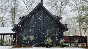 Una cabaña con techo pronunciado, rodeada de árboles cubiertos de nieve.