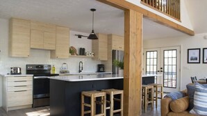 Cocina moderna con armarios de madera, una isla central, taburetes de bar y una zona de comedor con un sofá de cuero marrón.