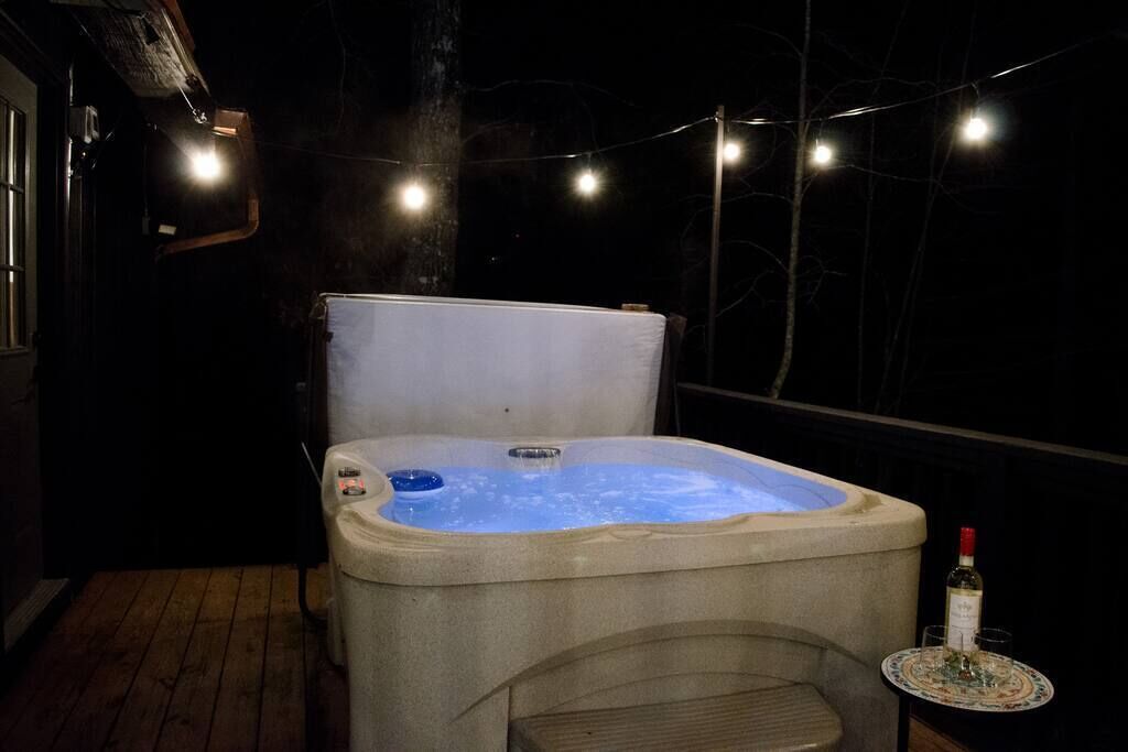 A hot tub with a table and a bottle of wine nearby, surrounded by string lights.