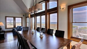 Ein Essbereich mit einem langen Tisch, mehreren Stühlen und großen Fenstern mit Blick aufs Meer.