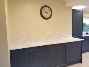 A kitchen with dark cabinets, a marble countertop, and a wall clock.