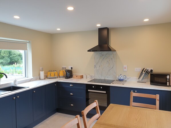 A modern kitchen with dark blue cabinets, a black range hood, a microwave, and a wooden dining table.