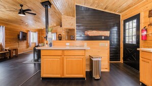 Ein Holzblockhaus-Interieur mit einer zentralen Holztrenne, einem Deckenventilator, einer schwarzen Wand und einem Feuerlöscher.