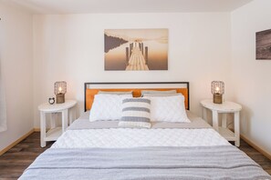 A bedroom with a wooden headboard, white bedding, two bedside tables with lamps, and a painting above the bed. - Grand Lake Getaway Near RMNP + Deck with Views! (Grand Lake)