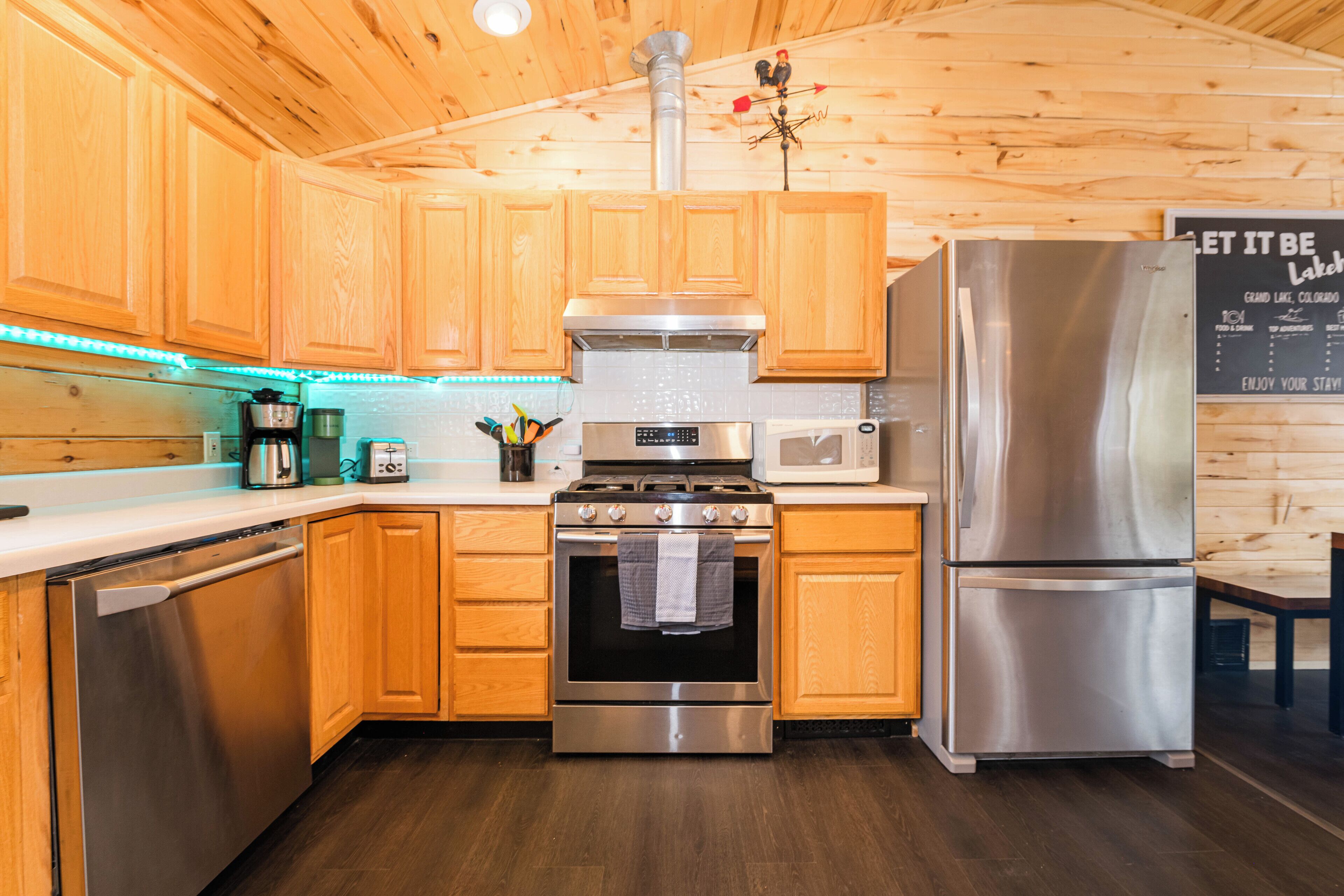 A modern kitchen with wooden cabinets, stainless steel appliances, and a chalkboard menu.