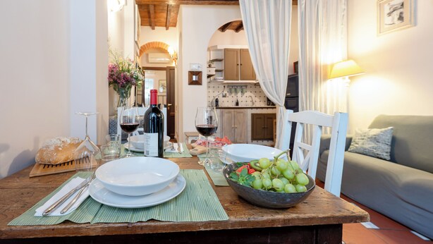 Una mesa de comedor dispuesta con platos, vasos y un bol de uvas, con techo de madera y un sofá al fondo.