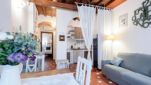 Una sala de estar acogedora con un sofá, una mesa de comedor con mantel de encaje y una cocina al fondo.