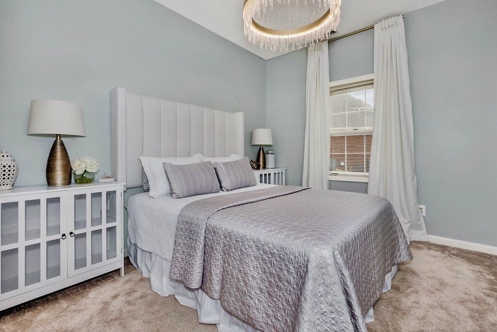 Une chambre à coucher avec un grand lit, une table de chevet, une lampe et une fenêtre avec des rideaux.