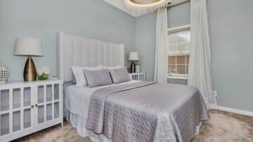Une chambre à coucher avec un grand lit, une table de chevet, une lampe et une fenêtre avec des rideaux.