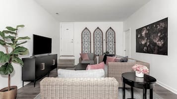 Un salon moderne avec un meuble TV noir, des meubles en osier et un grand tableau accroché au mur.