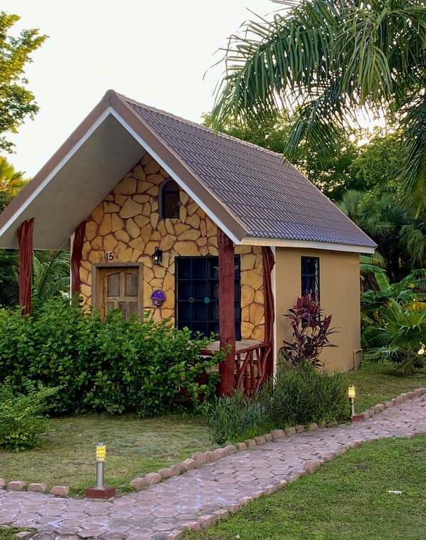 A stone house with a tiled roof, number 15, surrounded by lush greenery and a paved pathway. - El Gran Mestizo Resort (Orange Walk)